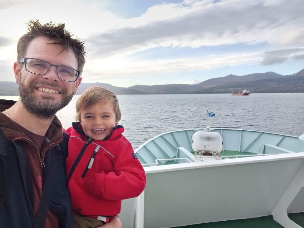 man holding boy, ferry, open water, mountains