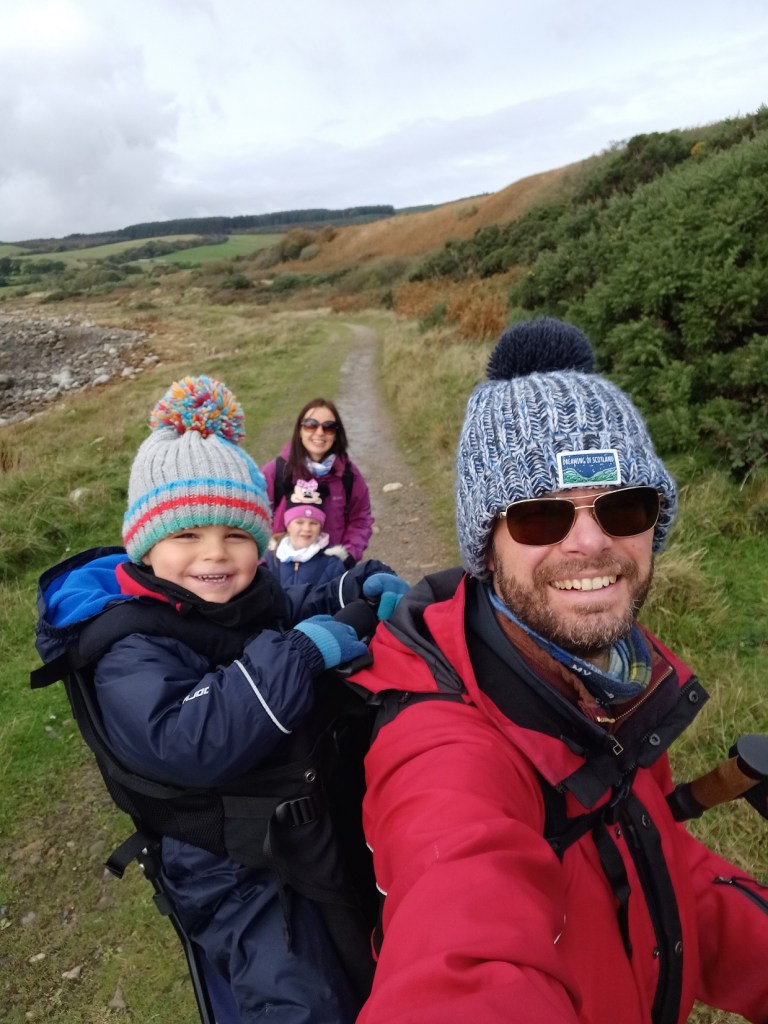 man carrying boy on his back, man and boy in hats, smiling people, hills, arran