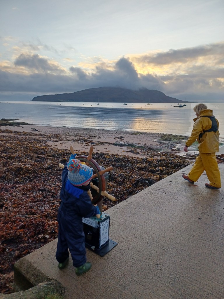 holy island, boy using steering wheel, fisherman, boats in water, open water,  sunrise